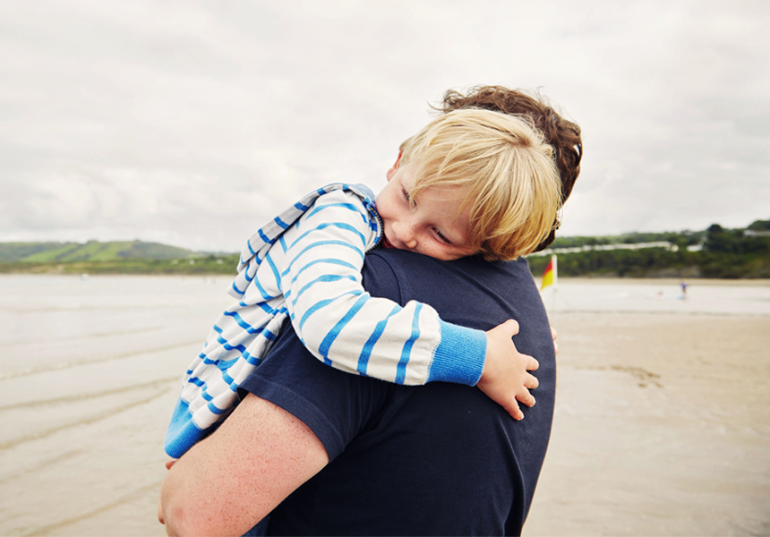 Little boy giving his Father a hug while at the beach together