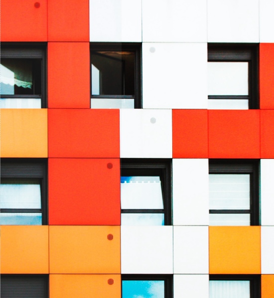 Un lateral de un edificio de apartamentos coloreado con formas geométricas en rojo, naranja y blanco.