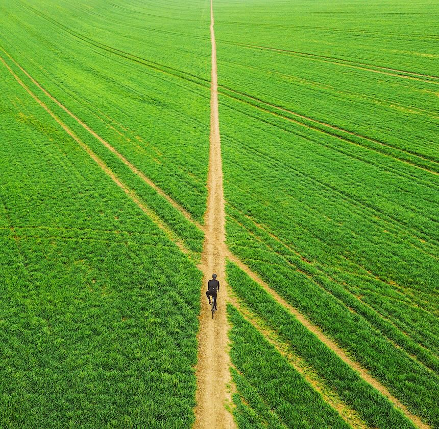 Personne marchant le long d’un sentier étroit à travers un vaste champ vert, vue de dessus.
