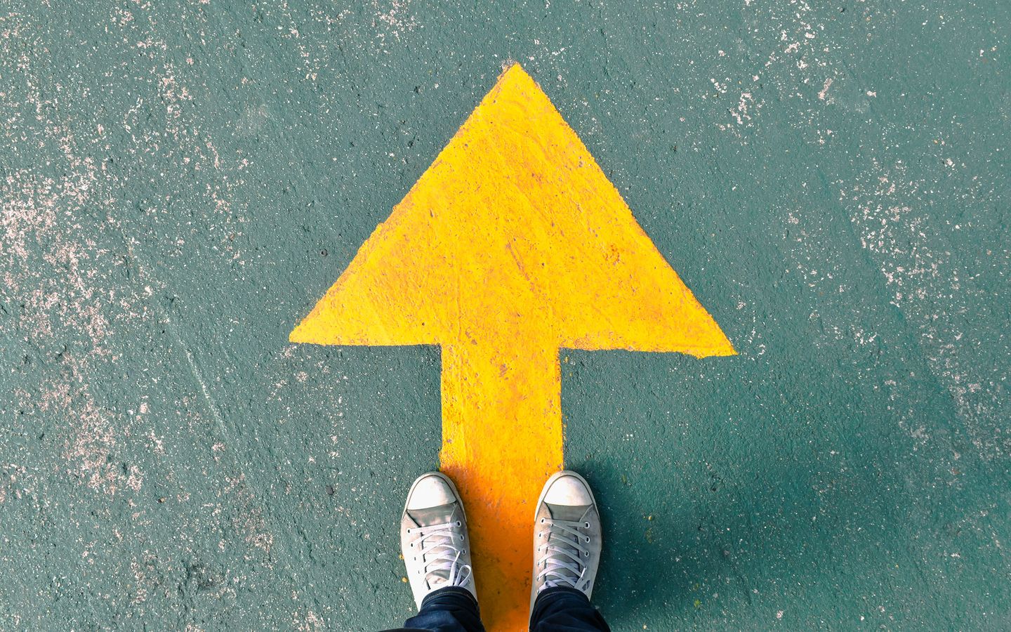 Person standing on asphalt next to a large yellow arrow pointing forward.