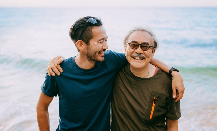 Asian man and his father smiling for a photo at the beach