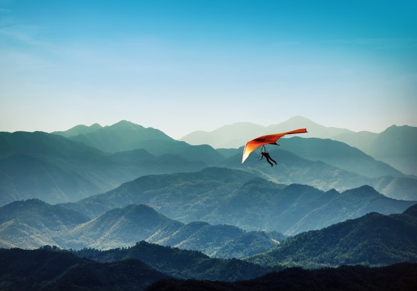 Hang glider soaring above wavy mountain ranges