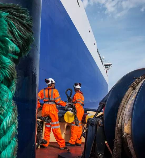 Tug workers on tug at sea with ropes in foreground