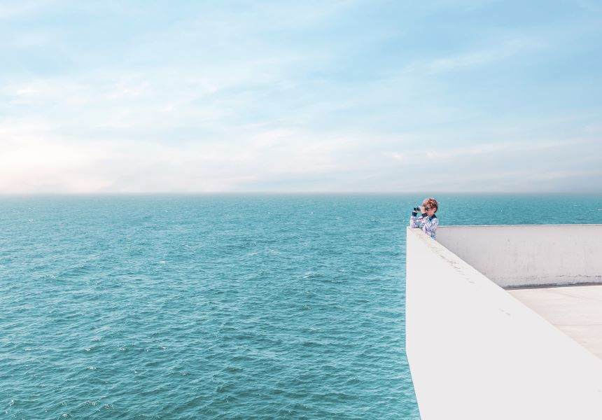 A boy looking at the sea with binoculars
