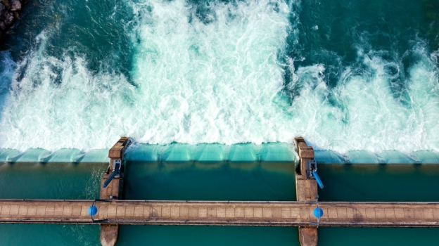 Water flowing over a concrete dam spillway with metal gates viewed from above