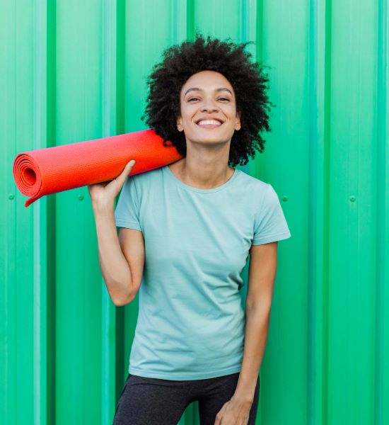 young person smiling holding a red yoga mat