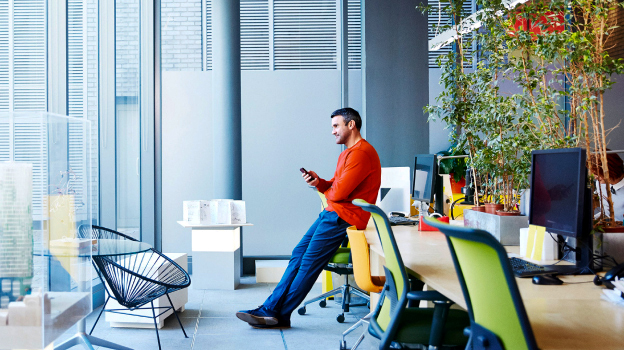 man in orange shirt leaning on desk with computers