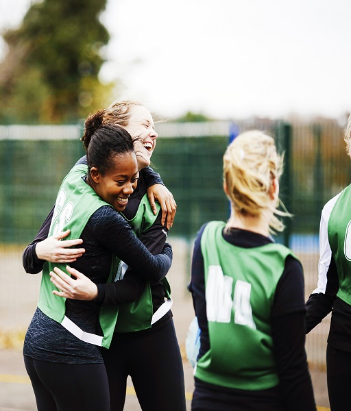 Two women hugging while playing outside in a larger group of friends