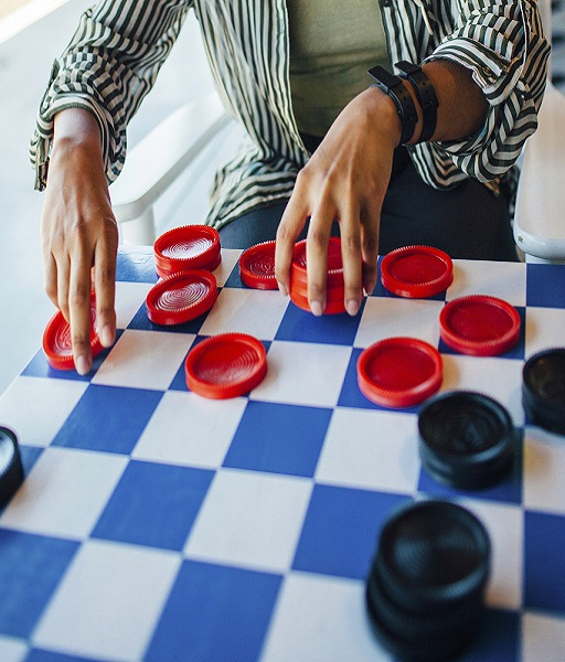 Hands are seen moving a piece on a checkers board 