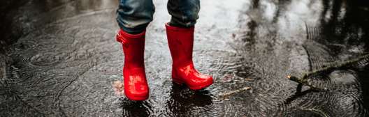 A figure in red boots braves the rain, representing the importance of emergency savings within retirement strategies