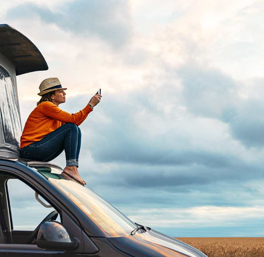 A woman perched on a car, using her cell phone, representing the exploration of retirement insights.