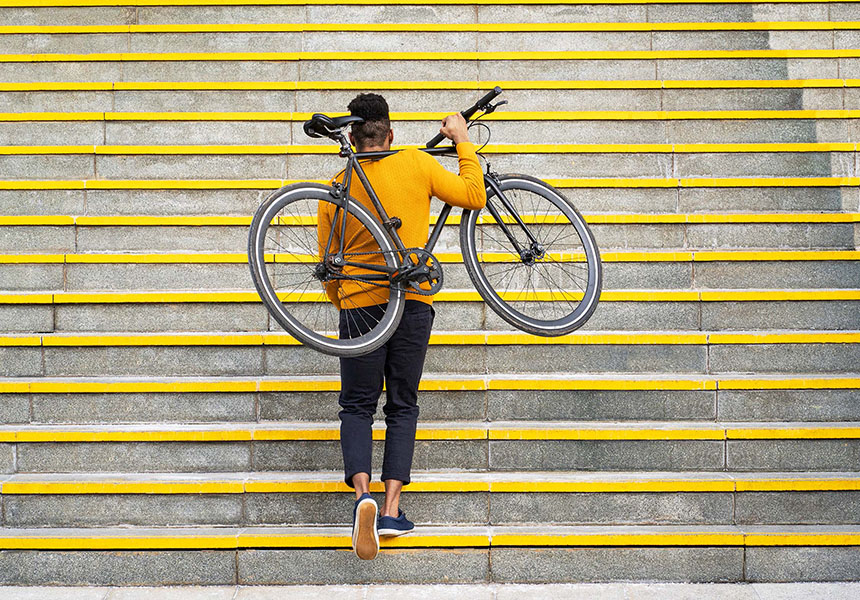 In an outside environment, a man is walking up stairs carrying his bicycle 