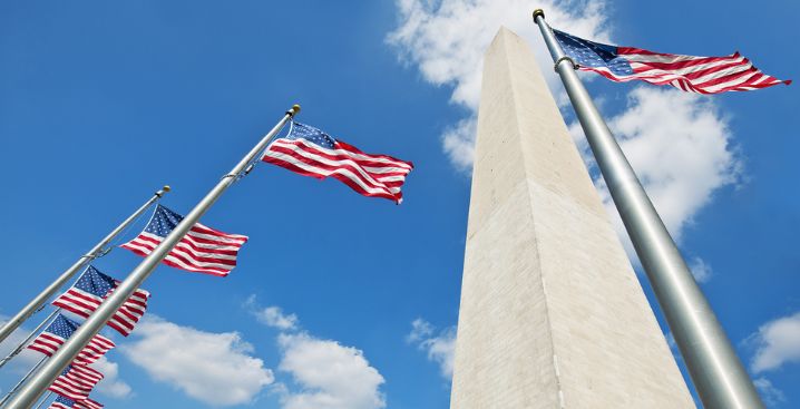 Upward view of the Washington monument with American flags against a blue sky.