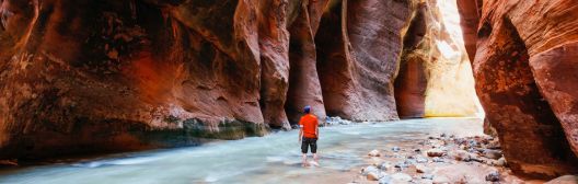 A man wearing an orange shirt stands in a narrow canyon, addressing key retirement income issues for plan sponsor