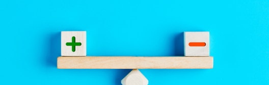 A balance holding plus and minus blocks against a blue wall