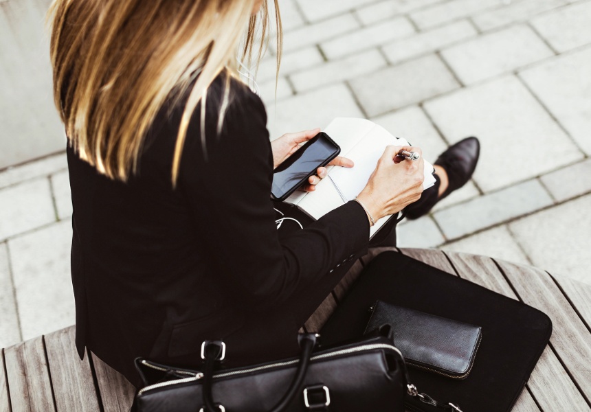 A business-suited woman sits on a bench, using her phone, representing the tools for effective retirement planning