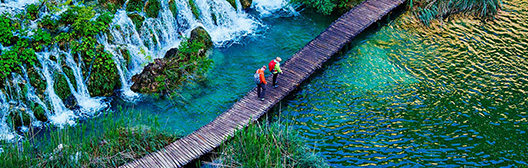 Hikers navigate a bridge over a waterfall