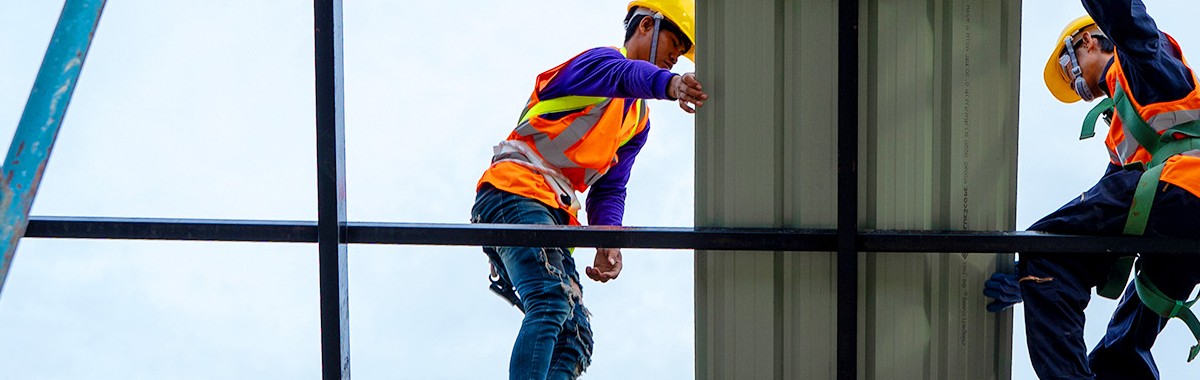 Construction workers in safety gear installing structural panels on a commercial building framework.