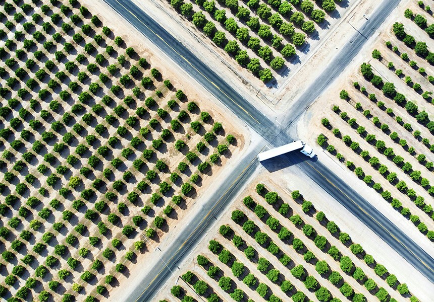 Aerial view of a truck crossing an intersection between rows of trees.