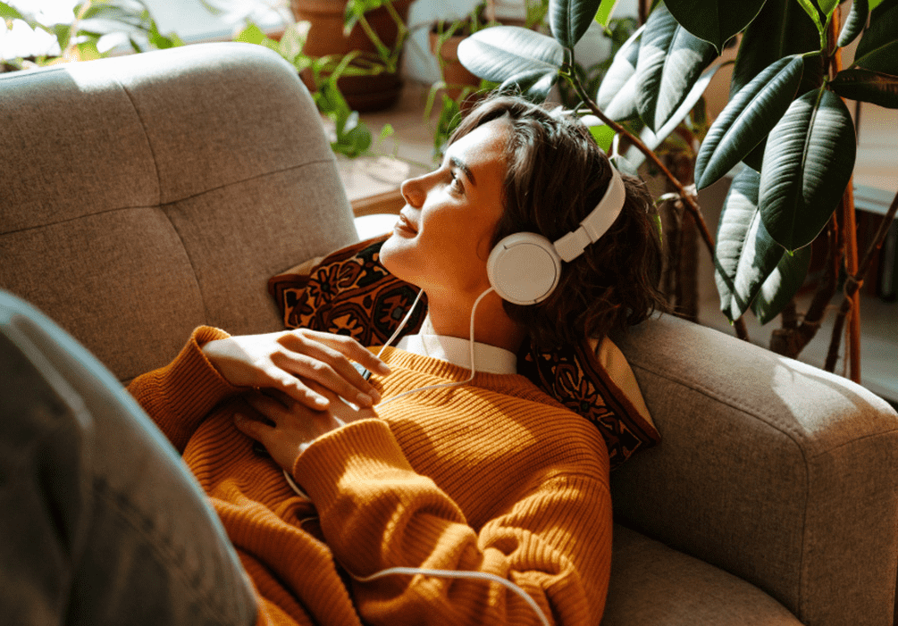 Imagen de una mujer tumbada en un sofá mientras lleva auriculares.