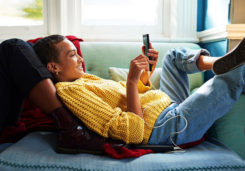 A woman is lying comfortably on a couch and looking at her mobile phone.