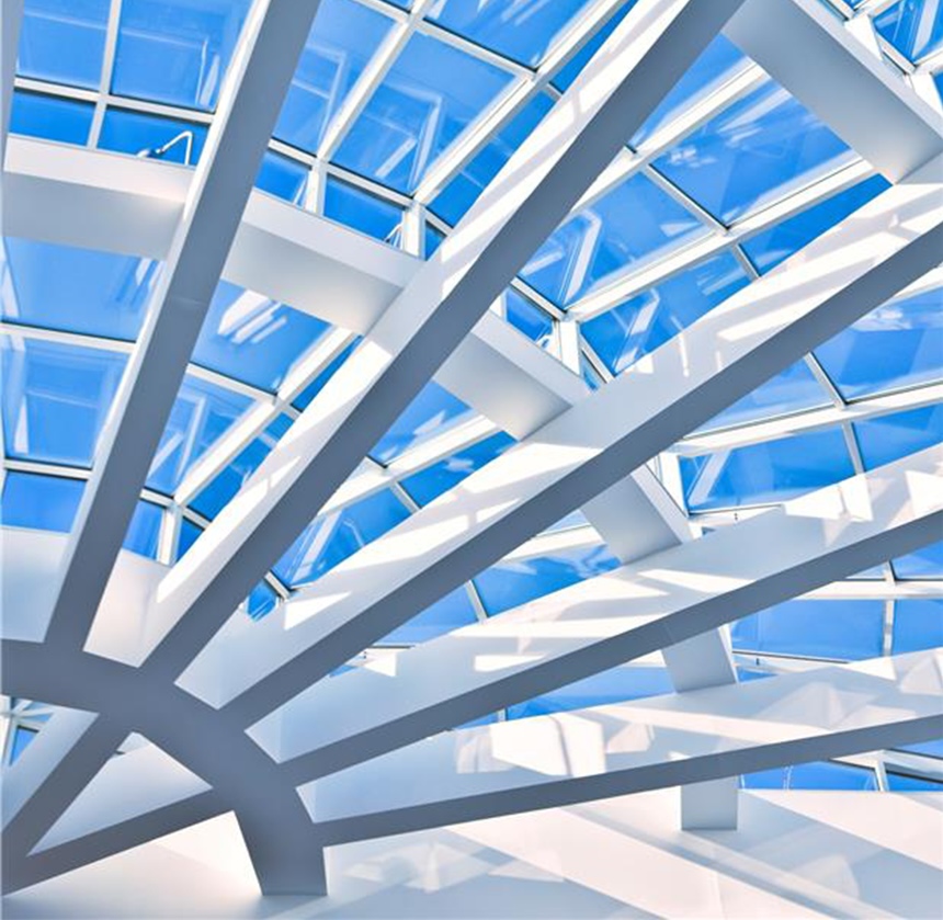 Nowoczesny sufit architektoniczny z krzyżującymi się białymi belkami i dużymi szklanymi panelami, nad którymi rozciąga się jasne błękitne niebo.