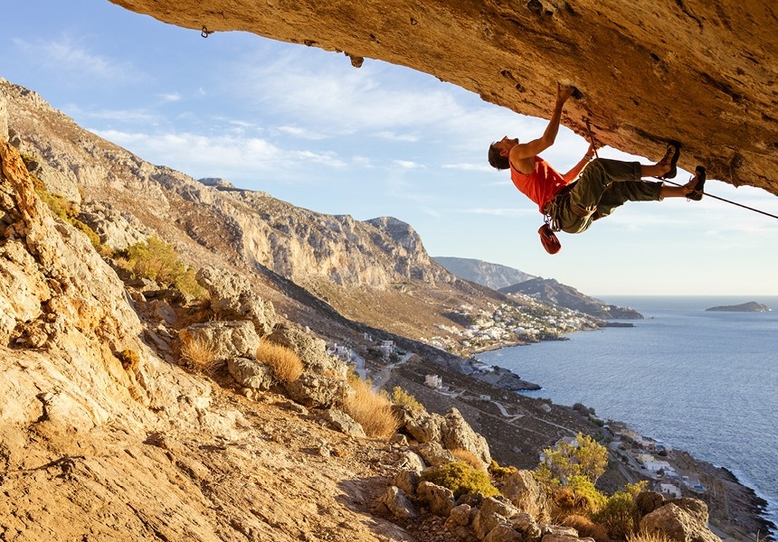 Person rock climbing on a cliff overlooking the sea.