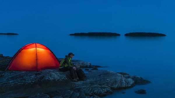 Person sitting beside an orange tent near water at dusk