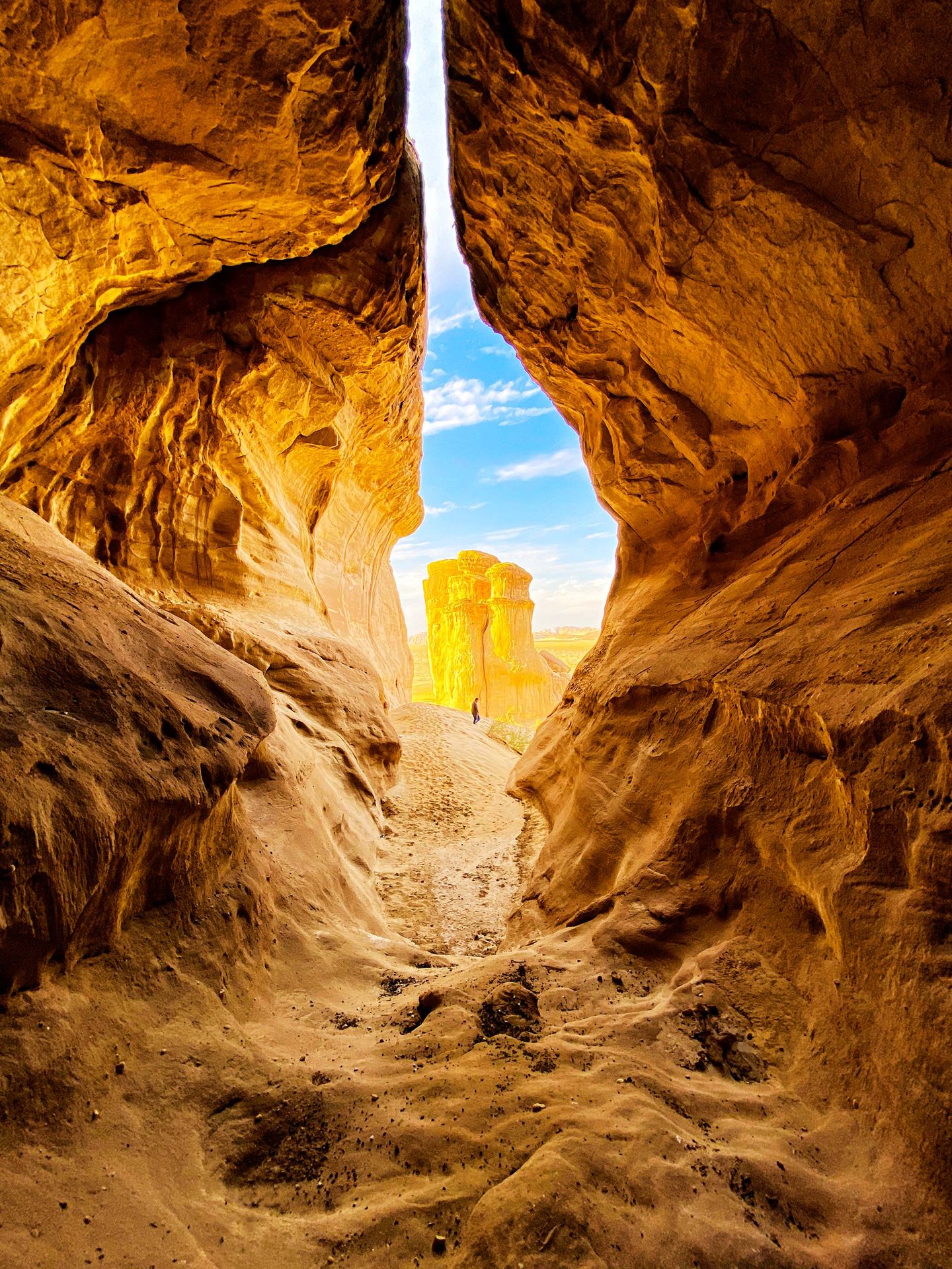 Sandstone canyon opening to a sunlit rock under blue sky.